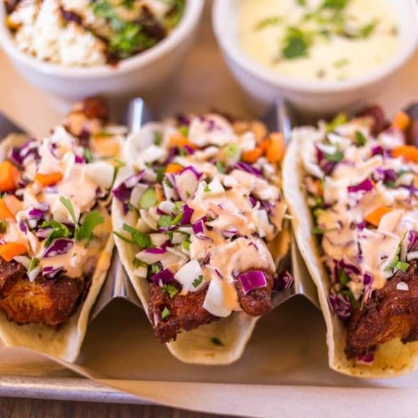Three Urbano Enchilada Taco Bar fish tacos with slaw and sauce, with two bowls of sides.